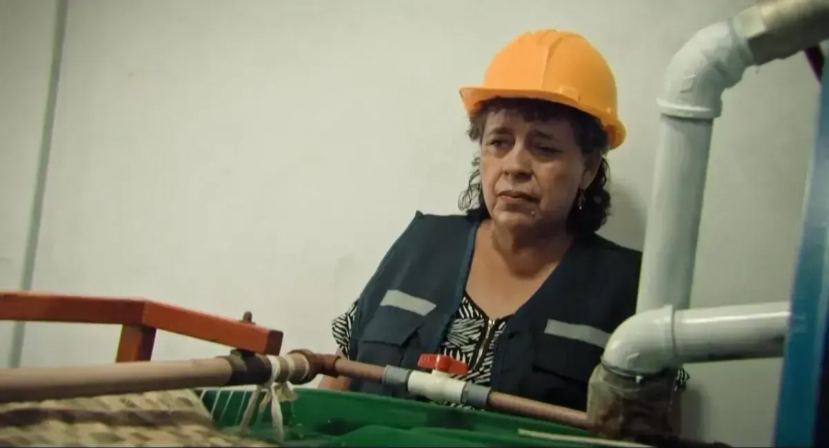 Retrato de una minera con casco naranja junto a tuberías