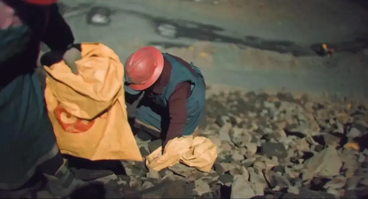 Minera con casco rojo llena sacos de piedra de noche