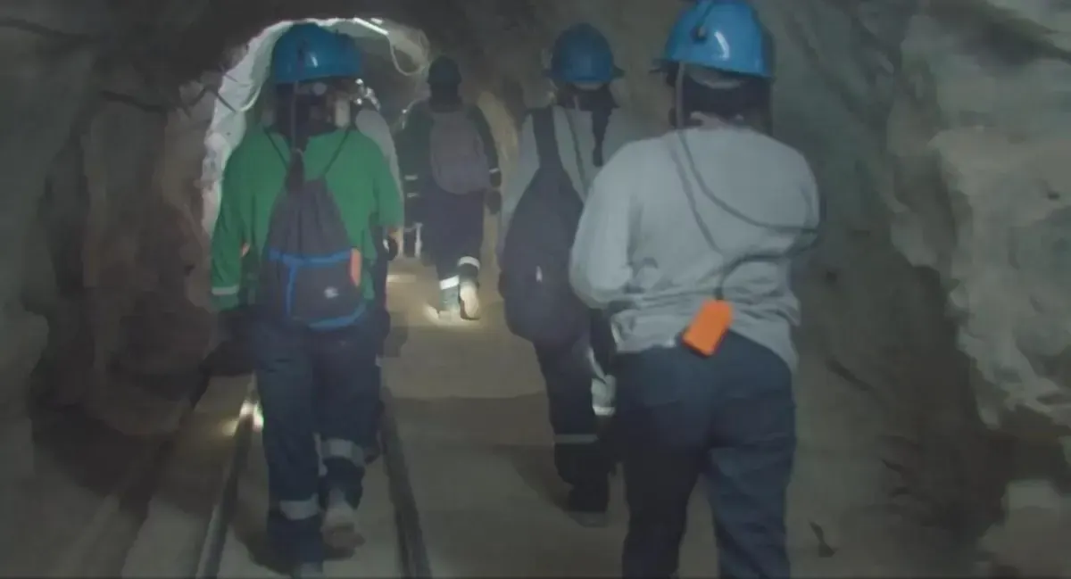 Mineras caminan dentro del socavón con cascos y linternas