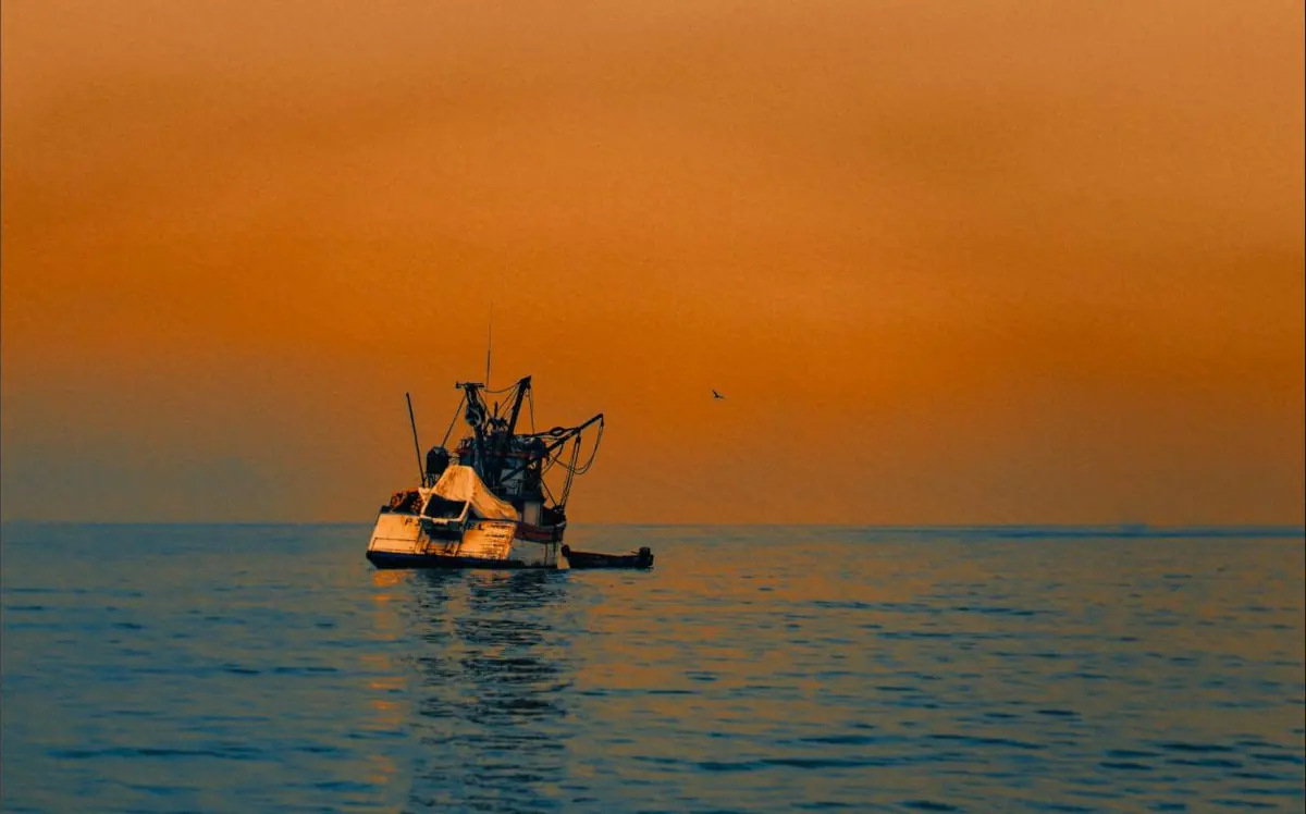 Barco pesquero solitario sobre un mar naranja