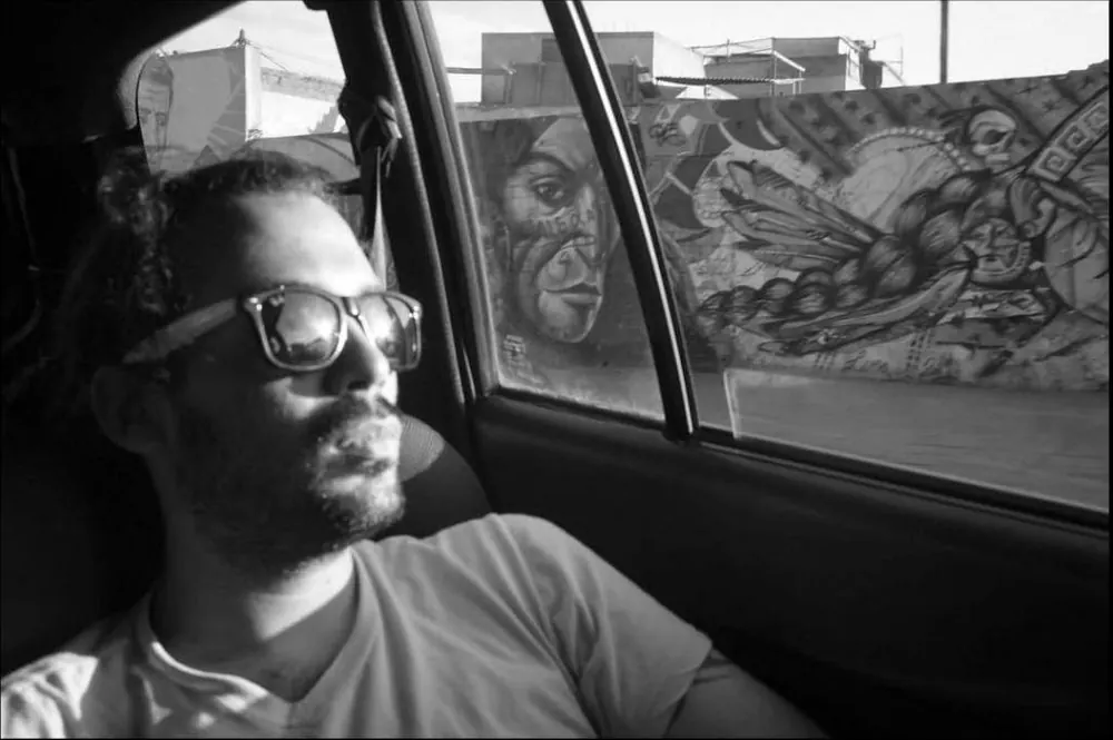 Jose Adrianzen dentro de un taxi frente a un mural, en blanco y negro